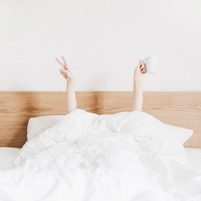 Young woman with coffee mug in bed with white linens. Minimal happy morning concept.